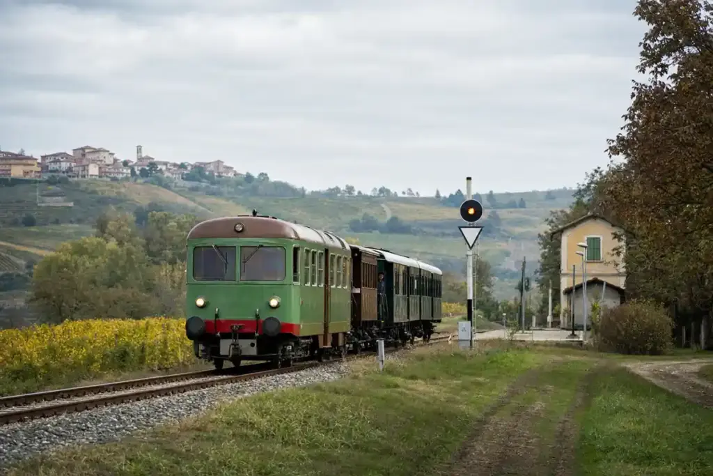 Treno storico verde su binari di campagna tra colline e vigneti, vicino a una piccola stazione
