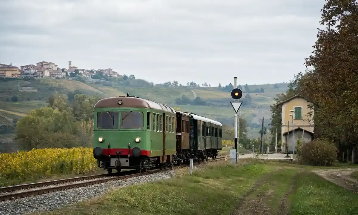 Treno storico verde su binari di campagna tra colline e vigneti, vicino a una piccola stazione