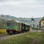 Treno storico verde su binari di campagna tra colline e vigneti, vicino a una piccola stazione