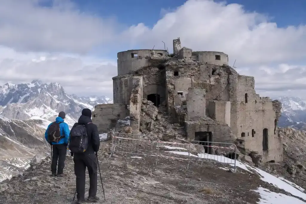 Due escursionisti davanti al Forte dello Chaberton in rovina, con transenne e nastro di divieto sulla vetta alpina