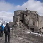 Due escursionisti davanti al Forte dello Chaberton in rovina, con transenne e nastro di divieto sulla vetta alpina