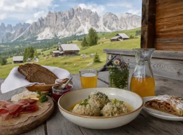 Pranzo tipico in baita con canederli, speck, pane di segale, formaggio e succo di mela con le Dolomiti sullo sfondo