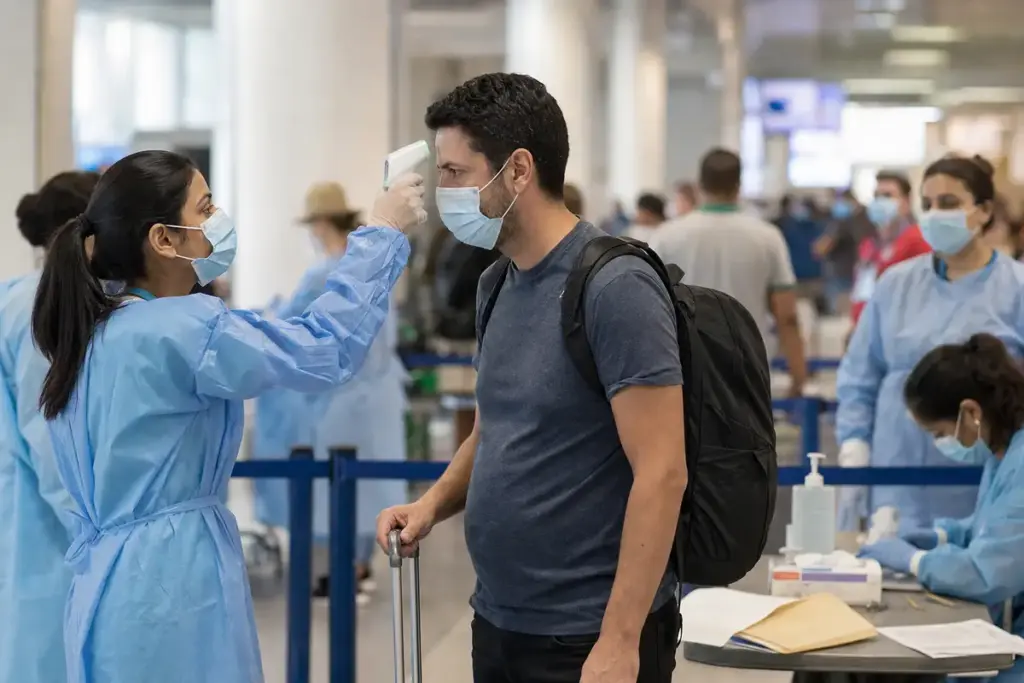Operatrice sanitaria misura la temperatura a un viaggiatore con termometro a infrarossi in aeroporto