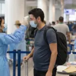 Operatrice sanitaria misura la temperatura a un viaggiatore con termometro a infrarossi in aeroporto
