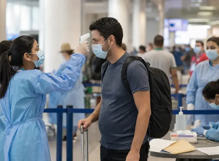 Operatrice sanitaria misura la temperatura a un viaggiatore con termometro a infrarossi in aeroporto