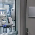 Laboratorio di embriologia visto attraverso una porta a vetri, con microscopio, banchi sterili e guanti blu sul tavolo