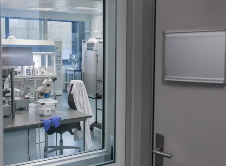 Laboratorio di embriologia visto attraverso una porta a vetri, con microscopio, banchi sterili e guanti blu sul tavolo