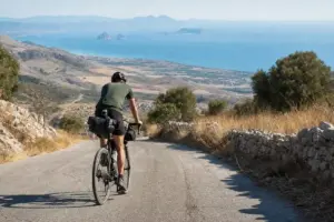 Ciclista con borse da viaggio pedala su una strada di montagna, con il mare e piccole isole sullo sfondo