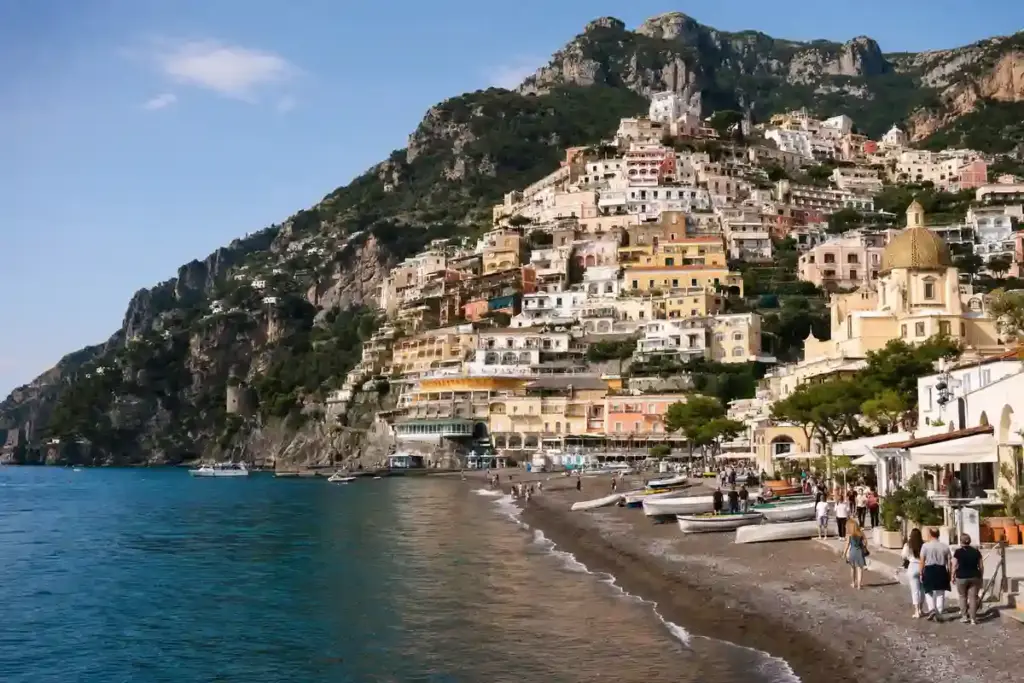 Positano sulla Costiera Amalfitana con case color pastello sul promontorio, spiaggia con barche e cupola della chiesa