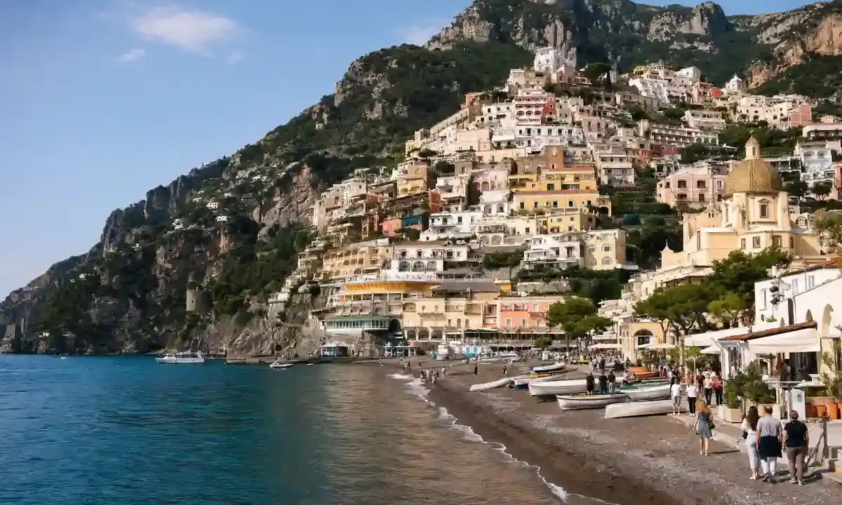 Positano sulla Costiera Amalfitana con case color pastello sul promontorio, spiaggia con barche e cupola della chiesa