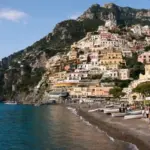 Positano sulla Costiera Amalfitana con case color pastello sul promontorio, spiaggia con barche e cupola della chiesa