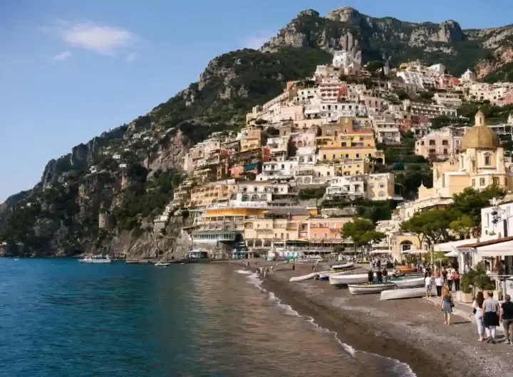 Positano sulla Costiera Amalfitana con case color pastello sul promontorio, spiaggia con barche e cupola della chiesa