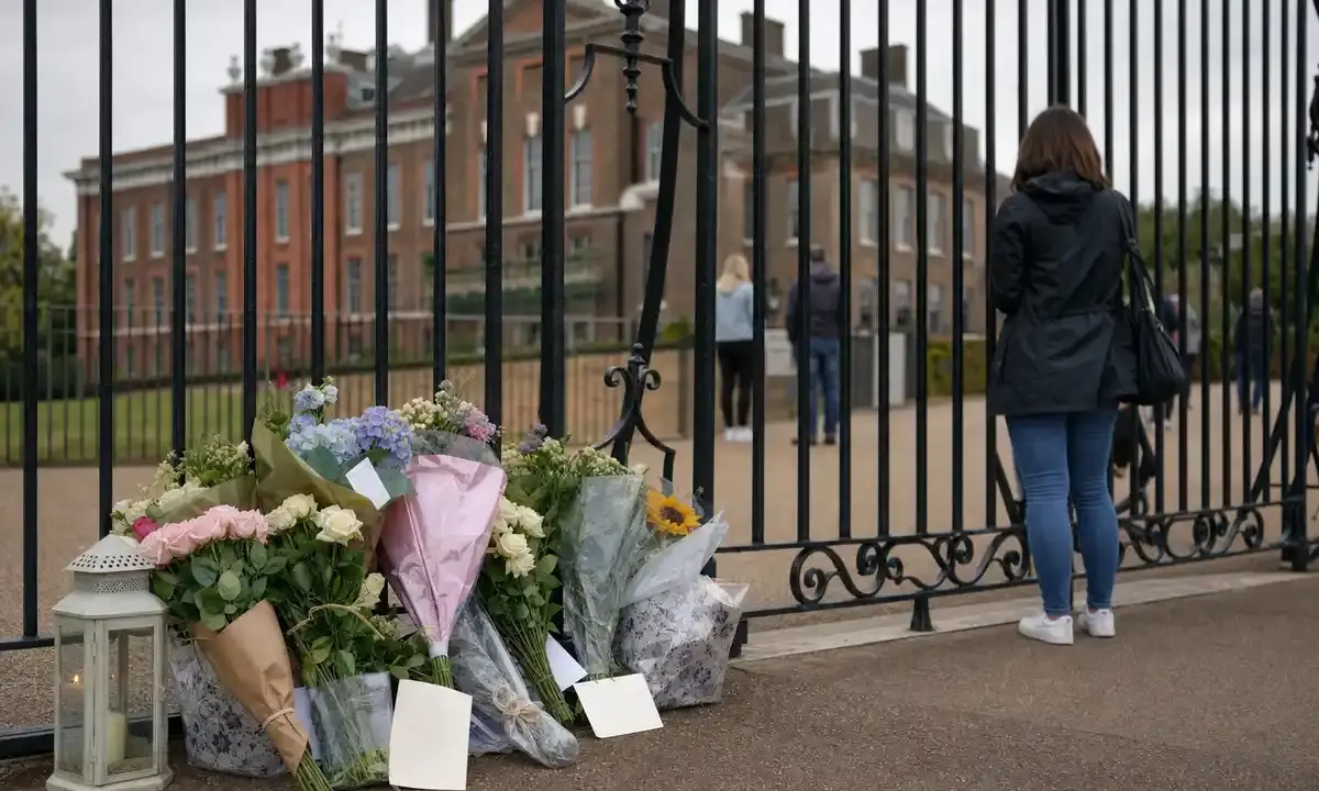 Mazzi di fiori e biglietti lasciati davanti ai cancelli di Kensington Palace, con visitatori sullo sfondo