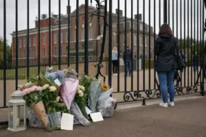 Mazzi di fiori e biglietti lasciati davanti ai cancelli di Kensington Palace, con visitatori sullo sfondo