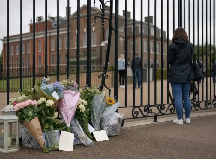 Mazzi di fiori e biglietti lasciati davanti ai cancelli di Kensington Palace, con visitatori sullo sfondo