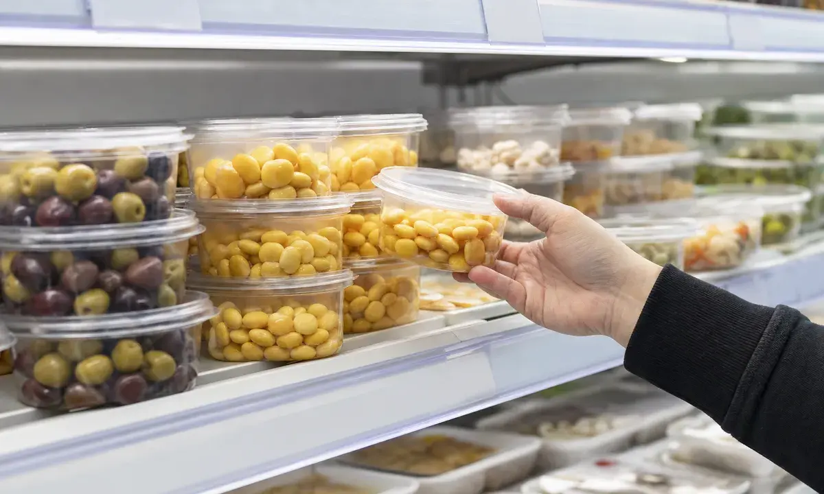 Mano di un cliente che prende una vaschetta di lupini gialli da uno scaffale refrigerato del supermercato