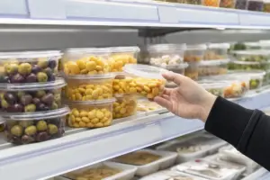 Mano di un cliente che prende una vaschetta di lupini gialli da uno scaffale refrigerato del supermercato