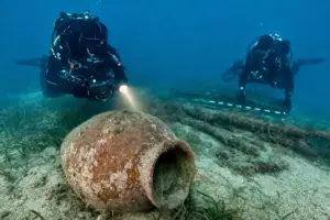 Subacquei documentano un grande dolium in terracotta sul fondale sabbioso, con posidonia e resti lignei sullo sfondo