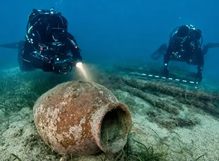 Subacquei documentano un grande dolium in terracotta sul fondale sabbioso, con posidonia e resti lignei sullo sfondo