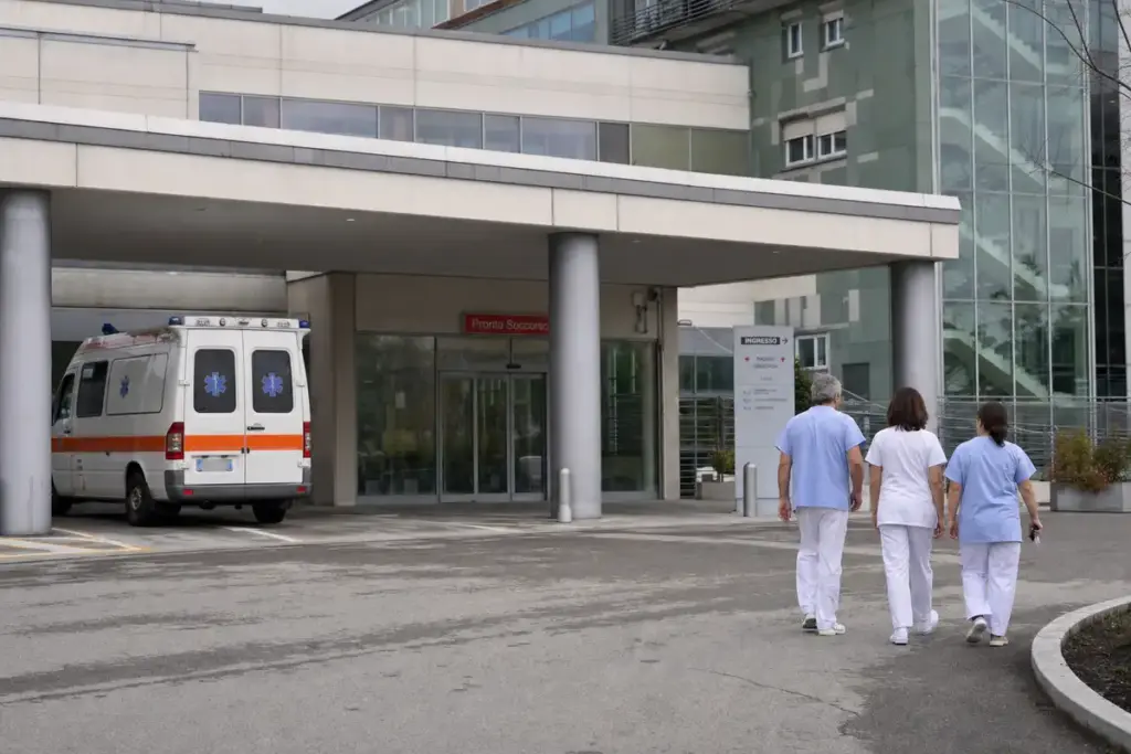 Ingresso del pronto soccorso di un ospedale con ambulanza parcheggiata e tre operatori sanitari che camminano