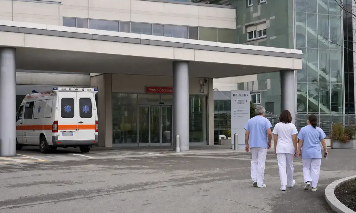 Ingresso del pronto soccorso di un ospedale con ambulanza parcheggiata e tre operatori sanitari che camminano
