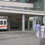 Ingresso del pronto soccorso di un ospedale con ambulanza parcheggiata e tre operatori sanitari che camminano