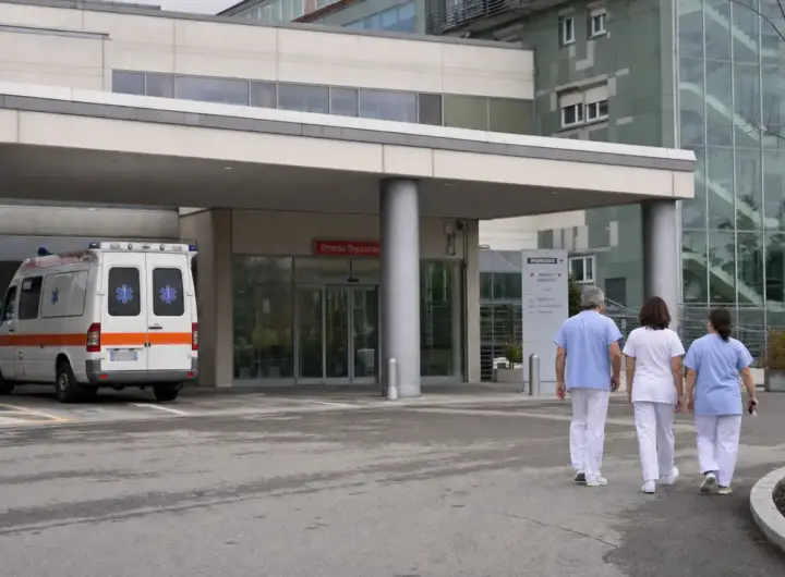 Ingresso del pronto soccorso di un ospedale con ambulanza parcheggiata e tre operatori sanitari che camminano