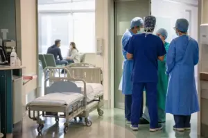 Corridoio ospedaliero pediatrico con lettino vuoto e personale sanitario in camice e mascherina che discute vicino a una