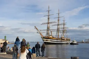Nave a vela a tre alberi in porto, con persone sulla banchina che osservano l’arrivo