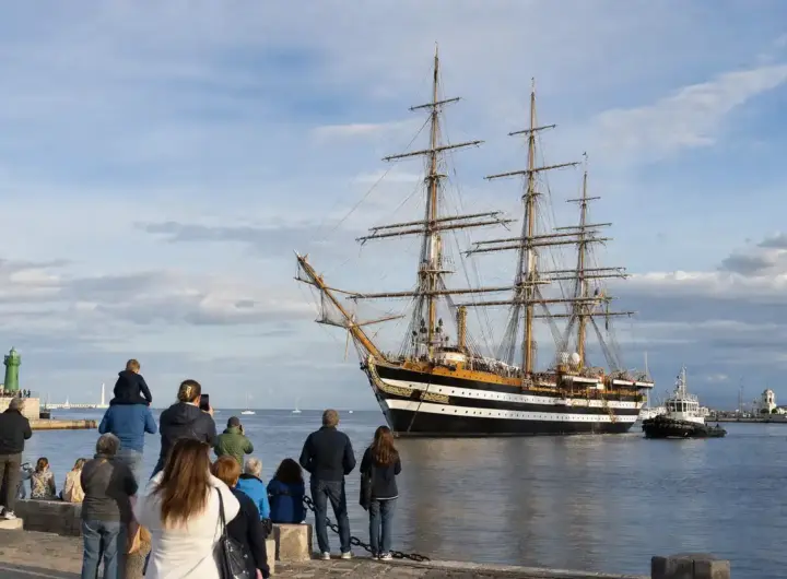 Nave a vela a tre alberi in porto, con persone sulla banchina che osservano l’arrivo