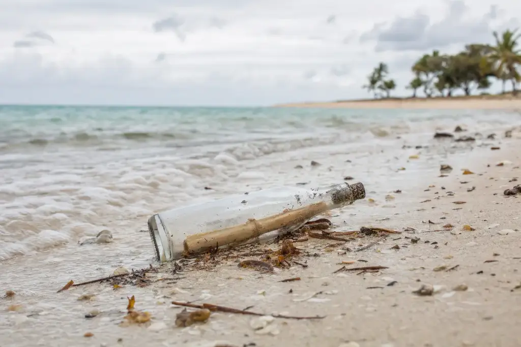 Bottiglia di vetro con un messaggio arrotolato sulla battigia di una spiaggia, con mare calmo sullo sfondo