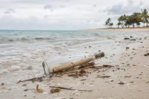 Bottiglia di vetro con un messaggio arrotolato sulla battigia di una spiaggia, con mare calmo sullo sfondo