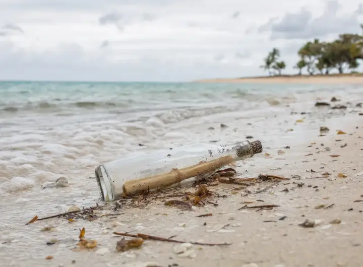 Bottiglia di vetro con un messaggio arrotolato sulla battigia di una spiaggia, con mare calmo sullo sfondo