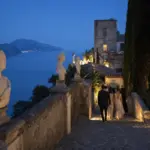 Ospiti eleganti scendono una scalinata in pietra tra busti in marmo con vista sul mare al tramonto