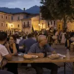 Sagra serale in una piazza di borgo abruzzese con tavolate, gente che cena e figuranti in costume sullo sfondo